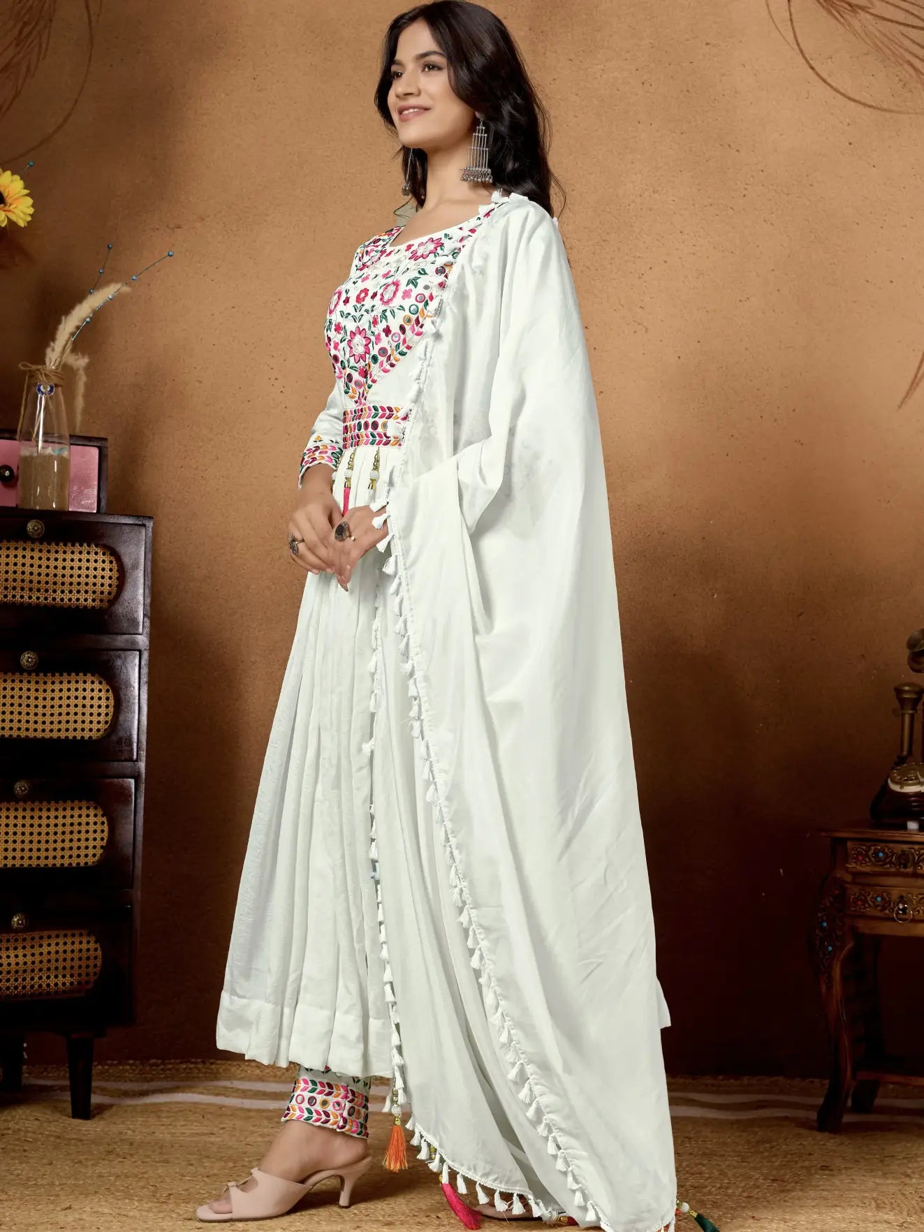 Woman in a white traditional outfit with floral patterns against a brown background