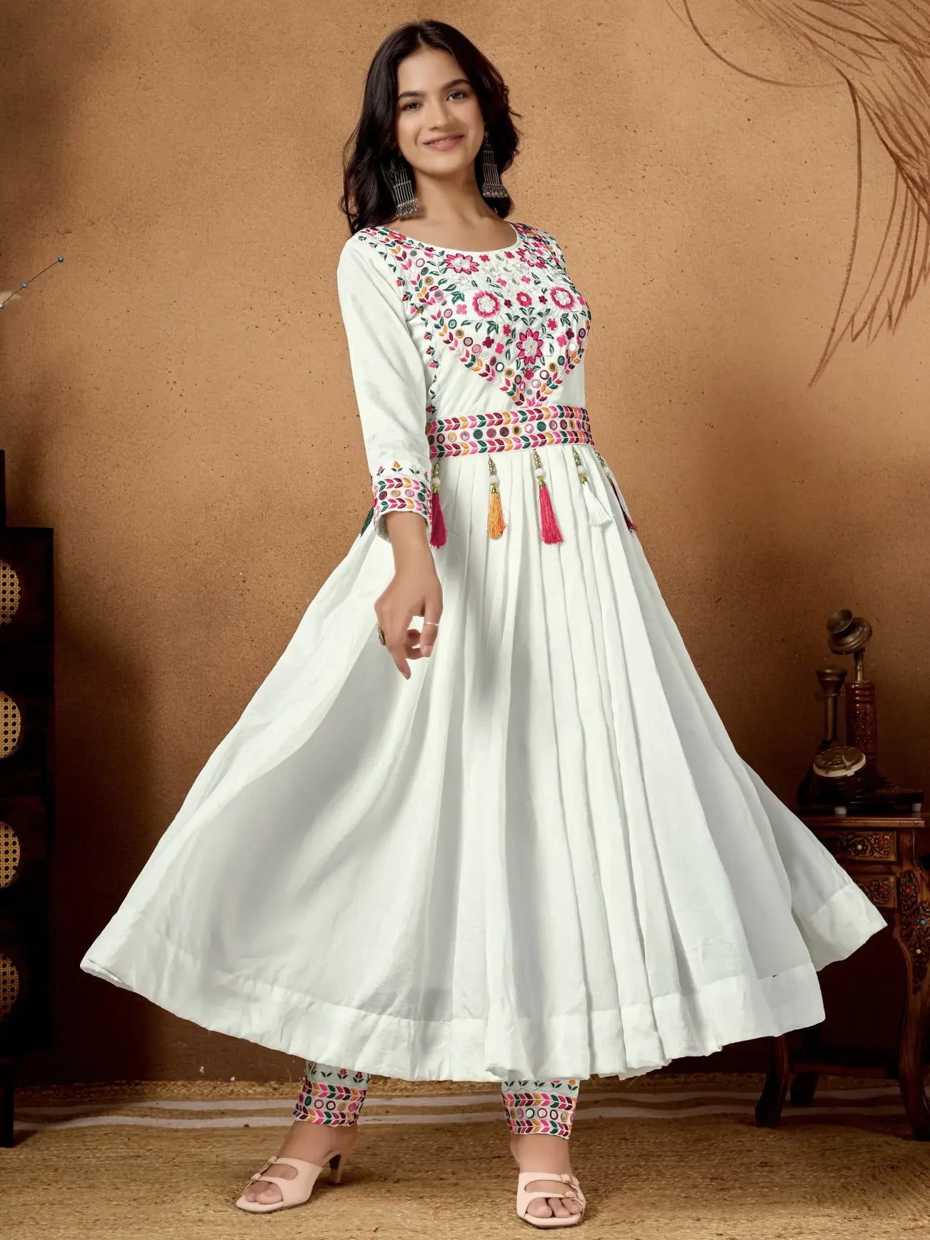 Woman wearing a white dress with colorful embroidery against a brown background