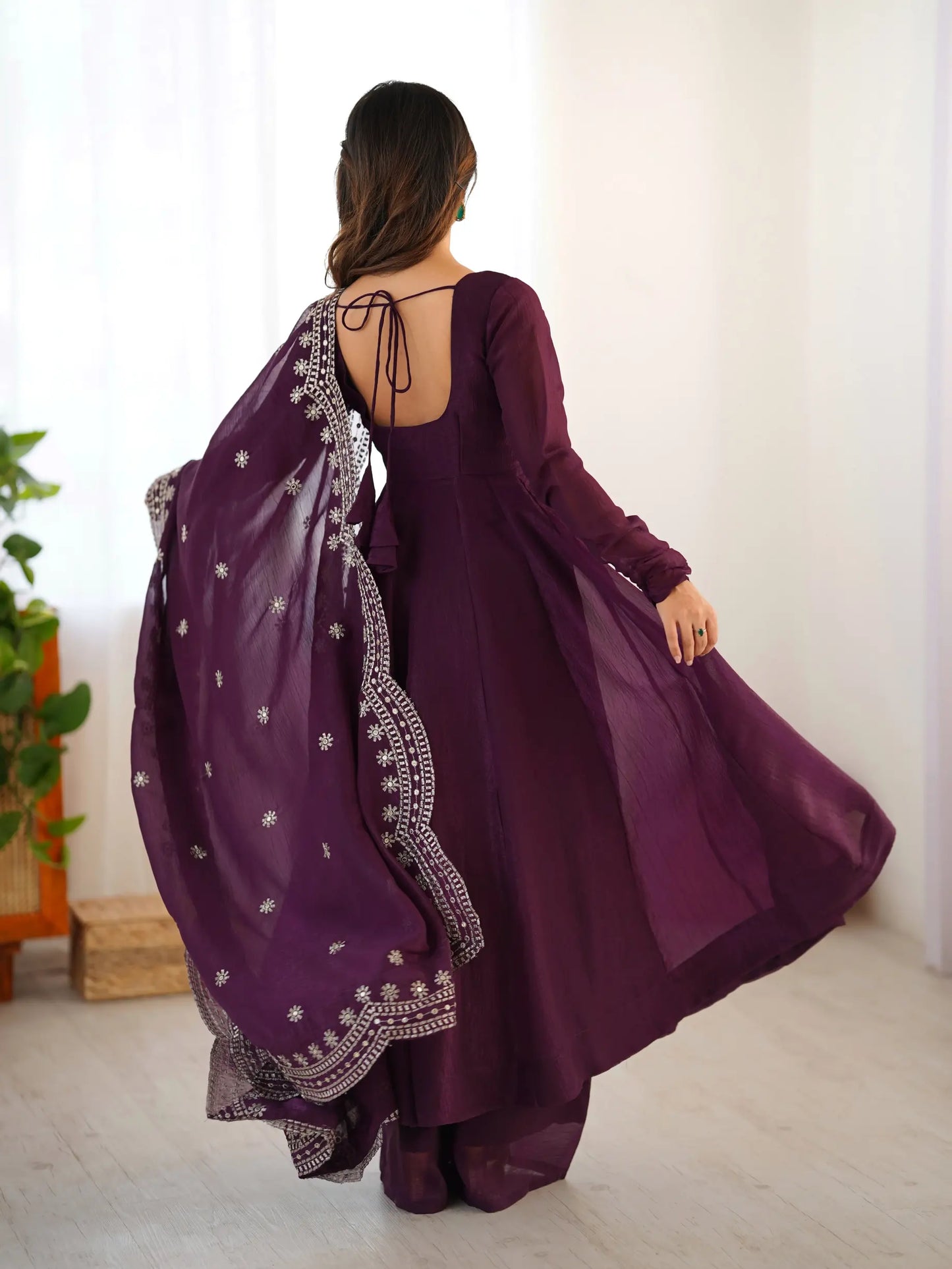 Woman wearing a purple traditional outfit with a matching dupatta in a minimal indoor setting.