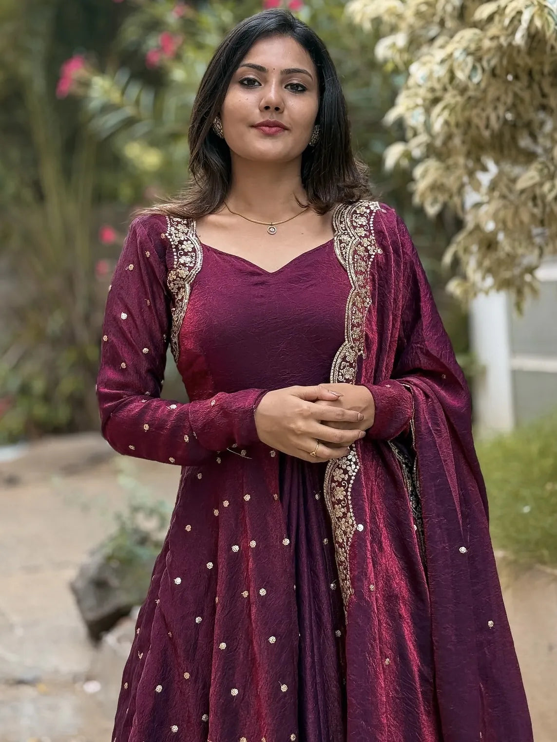 Woman wearing a wine traditional outfit with gold embroidery outdoors.