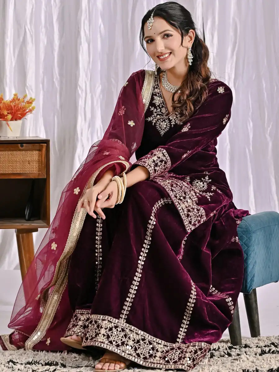 Woman in a wine embroidered Suit Set sitting on a chair with a white curtain background