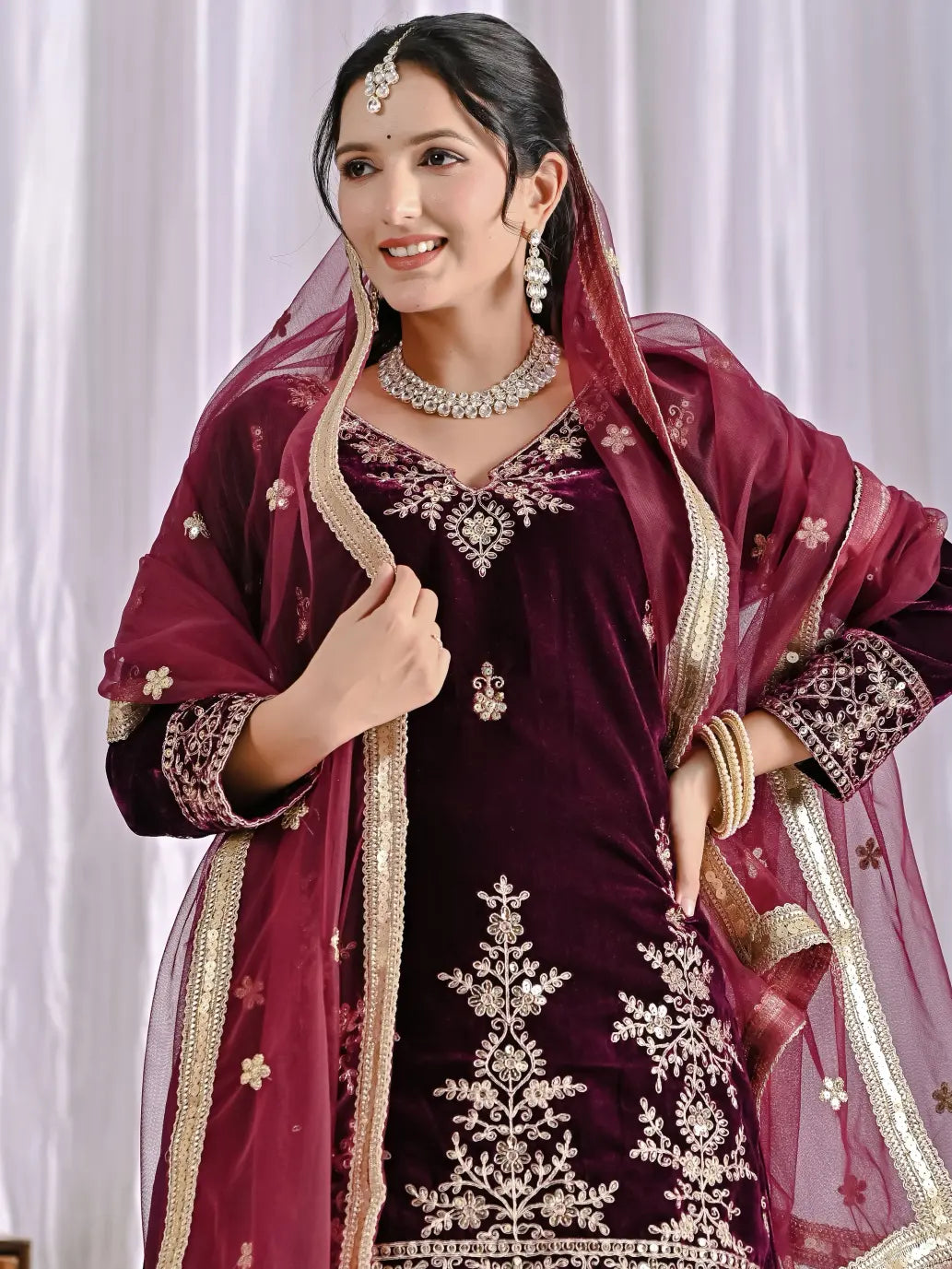 Woman in a wine traditional outfit with gold embroidery against a white background