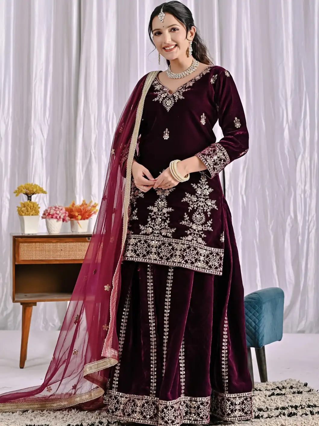 Woman wearing a dark purple traditional outfit with white embroidery in a room setting.