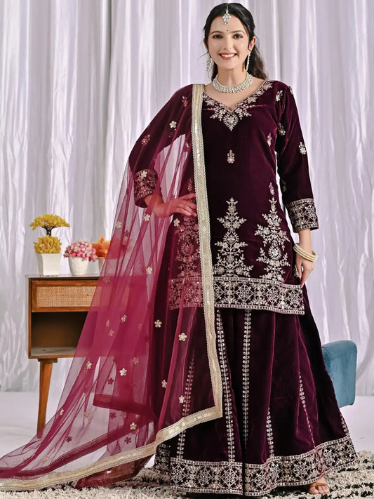 Woman wearing a wine embroidered traditional outfit with a pink dupatta against a white curtain background.