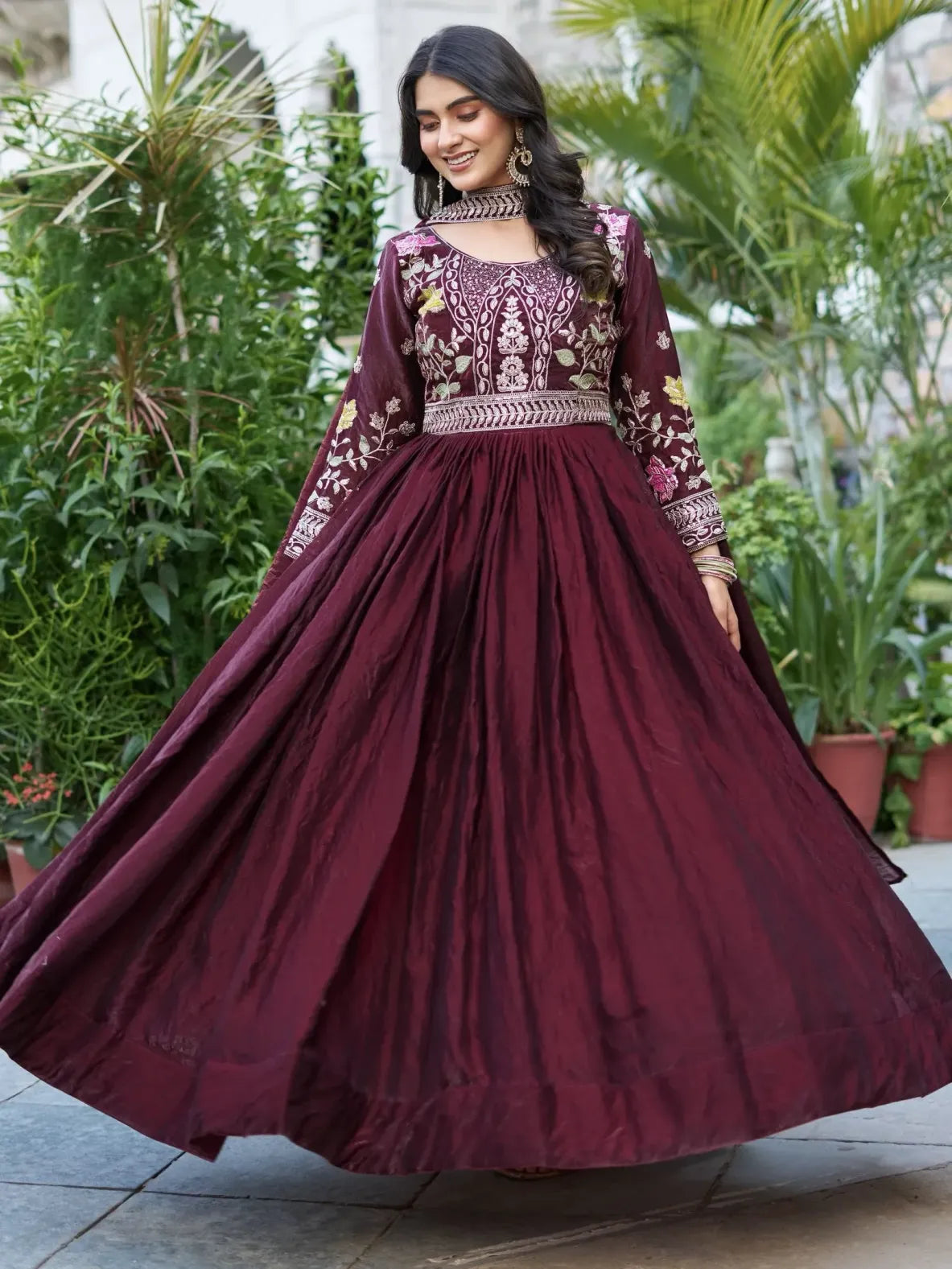 Woman in a maroon traditional outfit with floral embroidery standing outdoors.