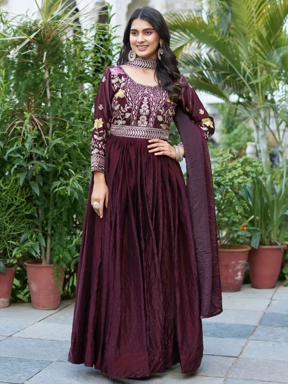 Woman in a maroon traditional outfit with floral patterns standing outdoors.