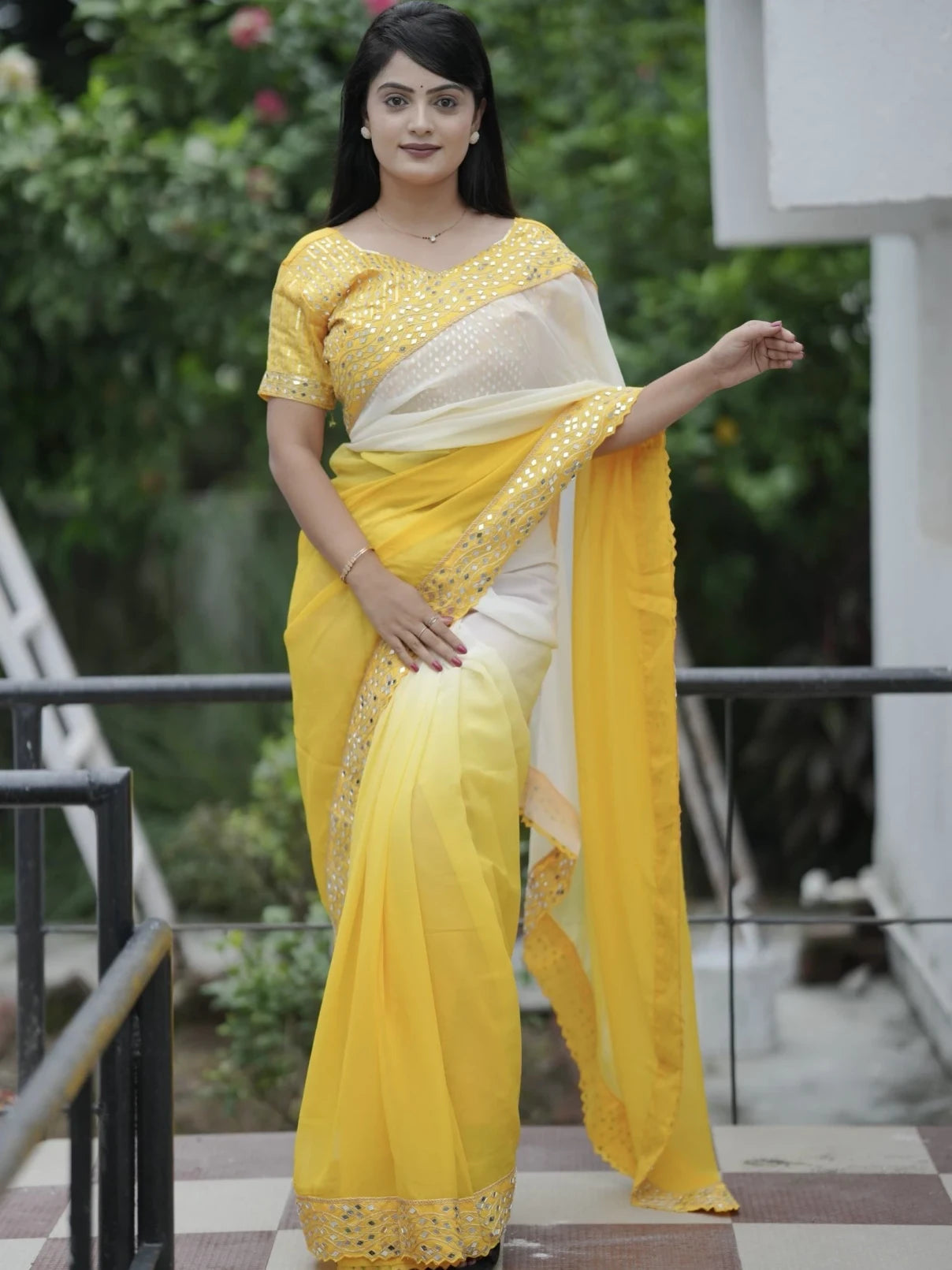 Woman wearing a yellow saree with a white blouse outdoors.